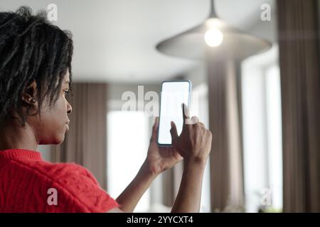 Over shoulder shot of African American woman looking at screen while setting brightness of kitchen bulb Stock Photo