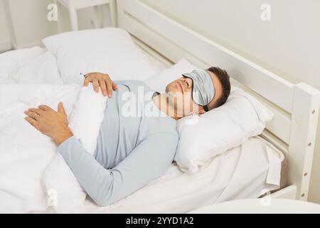 Young man in sleep face mask lying on bed sleeping in cozy modern bedroom in the morning. Stock Photo