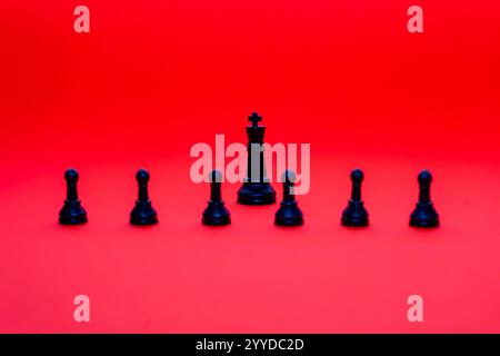 The arrangement features a black king surrounded by six black pawns on a vibrant red background. This composition highlights the contrast and importan Stock Photo
