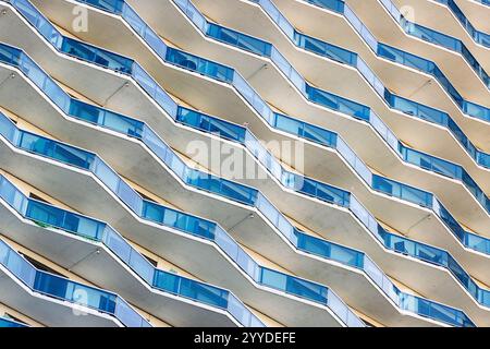 Rows of balconies with blue glass railings create a repetitive, geometric pattern on the building's facade. Sunlight casts shadows, emphasizing the wa Stock Photo