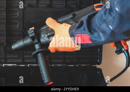Hands in protective gloves hold  a rotary hammer. worker, professional with hammer drill perforator. Stock Photo
