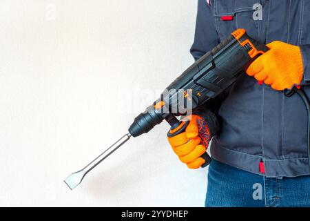 workman with a rotary hammer. Hands in protective gloves with hammer drill perforator. Copy space. Stock Photo