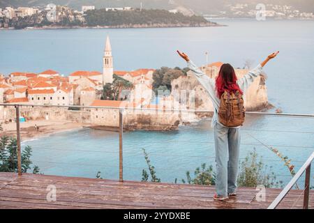 A smiling woman on holiday, casually strolling through an old town in Montenegro, with panoramic views and iconic architecture enhancing her travel ex Stock Photo