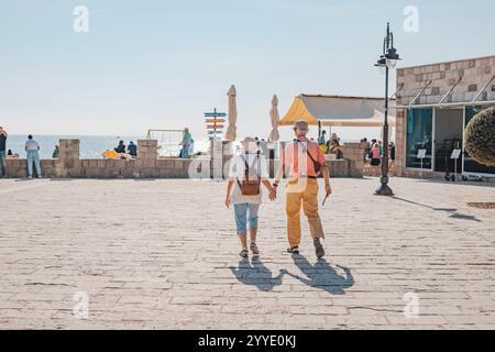 23 October 2024, Budva, Montenegro: Senior tourists holding hands walking on promenade by the sea Stock Photo