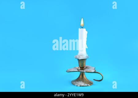 Very old retro candle in a candlestick with a burning flame on a classic blue background in a studio. Fire and minimalism concept with copy space Stock Photo