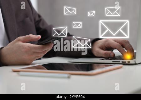 Man using mobile phone and laptop indoors, closeup. New message notification near device. Illustration of envelope Stock Photo