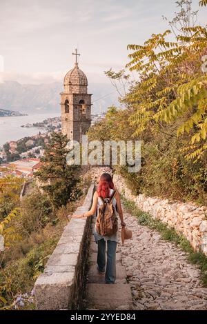 Female tourist walking down steps to church overlooking bay of Kotor in Montenegro during autumn Stock Photo