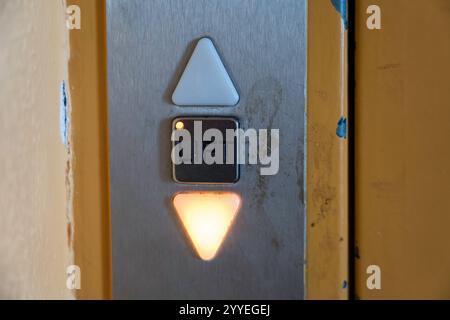 Worn Elevator Control Panel with Illuminated Down Arrow and Lift Button Stock Photo
