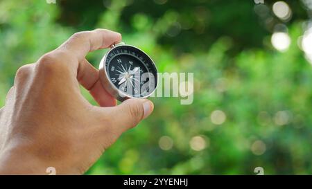 A hand holding a small compass against a blurred green foliage background. The concept of an adventurer seeking direction. Stock Photo