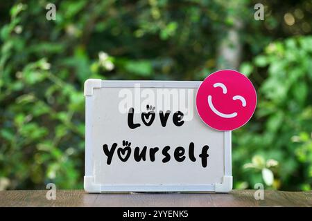 Chalkboard with Love Yourself writing and smiling face cards with blurred nature background. Mental health concept, appreciation, self-confidence Stock Photo