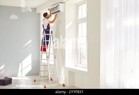 Professional male technician installing modern wall air conditioner in new house. Stock Photo