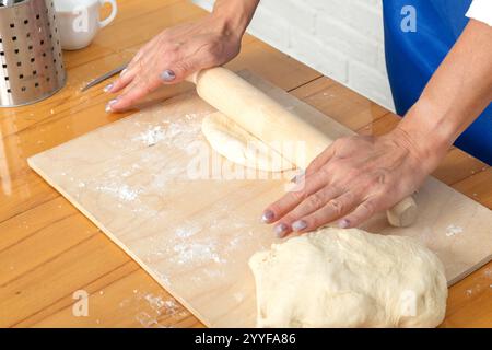 Female hands kneading dough on a wooden table in the kitchen Stock Photo