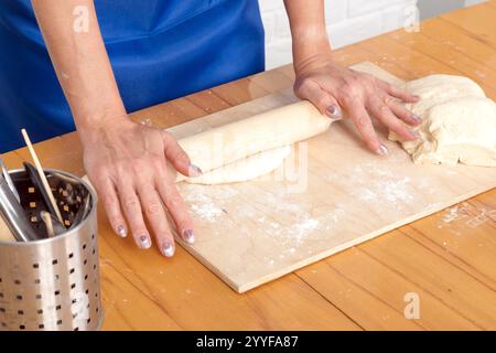 Female hands kneading dough on a wooden table in the kitchen Stock Photo