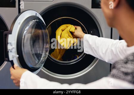 Over shoulder shot of man loading delicate cotton sweaters into washing machine refreshing clothes at coin laundromat, copy space Stock Photo