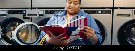 Website header shot of senior African American woman reading fashion magazine while waiting in self service laundry room with washing machines tumbling in background Stock Photo