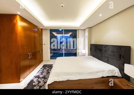 Bedroom with large bed for two persons against backdrop of glass sliding door with access to balcony Stock Photo