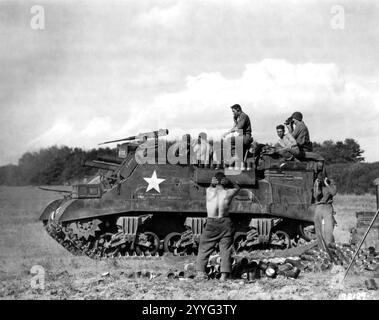 An M7 crew lets go with its 105 howitzer near Anet, France, its crew awaiting the blast before reloading. Empty shell casings indicate the rounds fired from this position. A Signal Corps cameraman photographs the action for newsreels. 20 August, 1944 Stock Photo