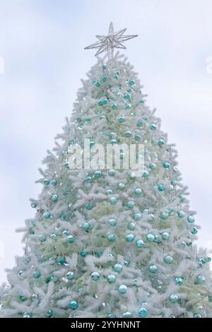Silver Christmas tree with turquoise New Year's toys. A star on the top of the tree against the sky. Stock Photo