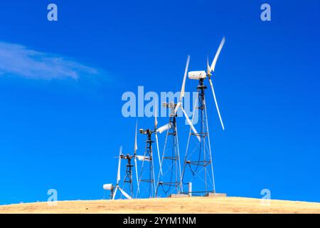 A row of wind turbines are on a hill, with the sun shining brightly in the background. The turbines are tall and spread out, with some of them being c Stock Photo