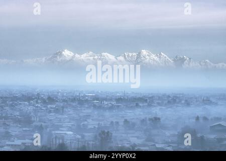 The city of Jalal-Abad is shrouded in morning mist, with the majestic Babash-Ata mountains rising in the distance Stock Photo