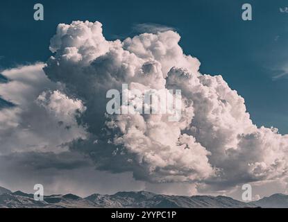 Dramatic cumulonimbus cloud forming above a mountain range, creating a stunning contrast between the bright white clouds and the dark blue sky Stock Photo
