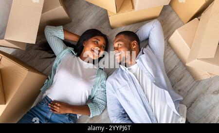 Loving black family with carton boxes around, lying on floor and having rest on moving day, top view Stock Photo