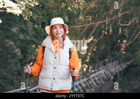 Female hiker enjoying a scenic walk through a lush forest, equipped with trekking poles and a backpack Stock Photo