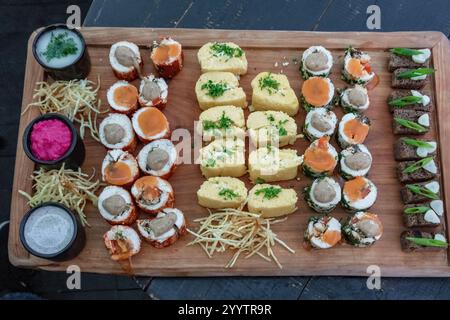 A wooden tray with a variety of sushi rolls and other food items. The tray is set up for a party or gathering Stock Photo