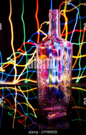 Glass Bottle Surrounded by Multicolored Light Trails on Black Stock Photo
