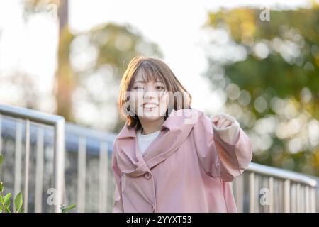 A woman in her 20s is smiling in a large park with nature in Handa City, Aichi Prefecture in autumn. Stock Photo