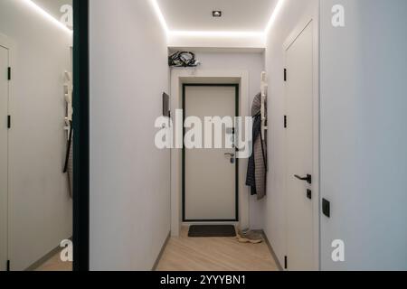 Modern hallway interior. White walls, wood floor, black door, full-length mirror, coats hanging. Minimalist design. Stock Photo