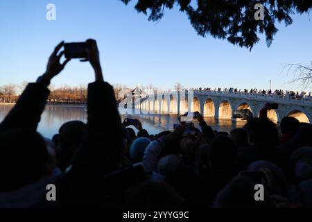 Beijing,China.21th December 2024. The golden red sunset light shines through the 17 arches of the bridge at the Summer Palace in Beijing, December 21, 2024. That day is Winter Solstice, one of the 24 solar terms in China. The 17-arch Bridge is famous for its “golden light piercing the arches” spectacle. Credit: Wang Ziru/China News Service/Alamy Live News Stock Photo