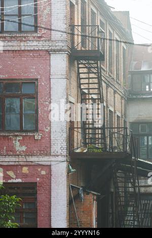 Old brick factory building with metal fire escape and peeling plaster. Urban architectural photography with weathered textures. Design for posters, ba Stock Photo