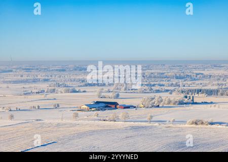 Aerial view of a snowy rural farmstead with frost-covered trees and ...