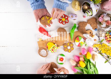 Family preparation for Easter. Holiday baking background, woman and child hands decorate homemade cookies with sugar glaze, in form of Easter symbols Stock Photo