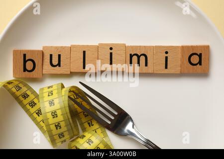 Plate with word Bulimia, fork and measuring tape on beige background, top view Stock Photo