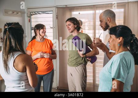 Diverse group of sporty people talking, laughing. Resting and drinking mate after yoga class in a friendly social atmosphere at the yoga club. Stock Photo
