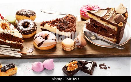 Selection of various cake pieces, macaroons, meringues, cookies and donuts on a wooden desk. Top view. Confectionery background. Stock Photo