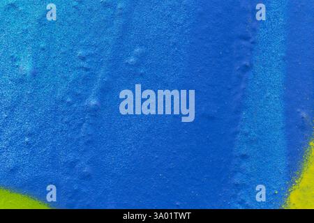 Macro close-up of a wall spray painted in light blue, blue and some yellow. Abstract full frame textured splattered graffiti background, copy space. Stock Photo