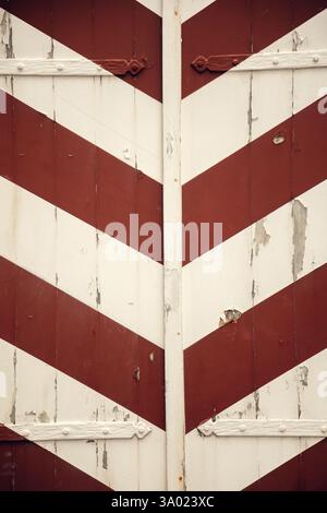 Vintage wooden shutters with diagonal red and white stripes. Close-up of weathered wooden shutters featuring. The peeling paint and rustic hinges add Stock Photo