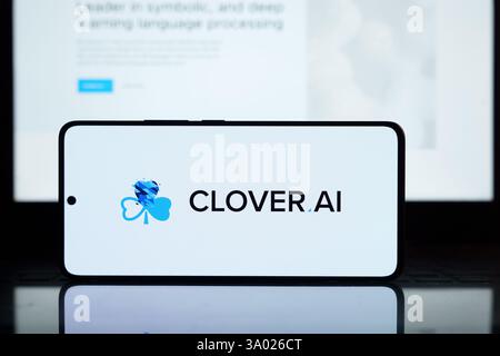 Smartphone screen shows CLOVER AI logo. Background displays website text. Modern tech, AI concept. March 2, 2025 Stock Photo