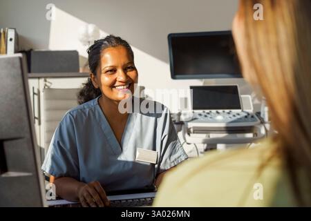 Smiling female obstetrician talking with patient while sitting in medical clinic at hospital Stock Photo