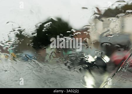 Blurred close up view of rain on a car windscreen, with town traffic in the background, UK. Stock Photo