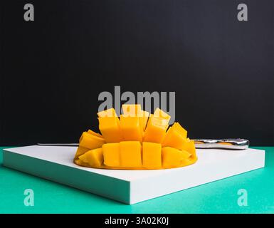 Bright yellow mango cubes are neatly cut and displayed on a clean white cutting board, highlighting the fruit's juicy texture and vibrant color. Stock Photo