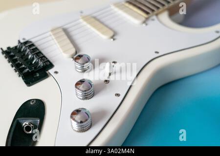 Close-up of the controls and pickups of a white electric guitar. Three chrome vo-lume and tone knobs, a five position pickup selector, single coil pic Stock Photo