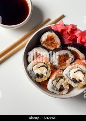 Sushi rolls in a bowl with pink ginger and soy sauce and wooden sticks on white table close up Stock Photo