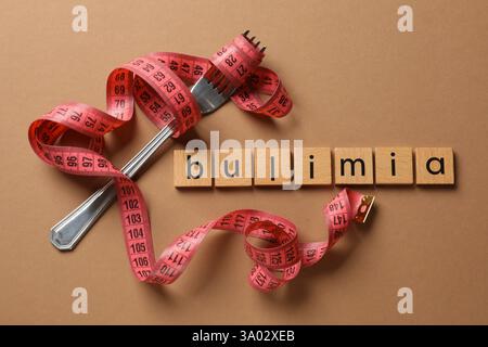 Word Bulimia, fork and measuring tape on brown background, top view Stock Photo