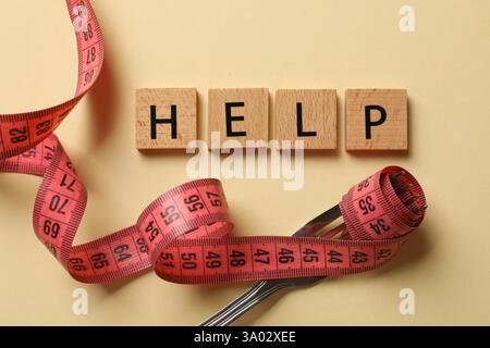 Bulimia. Word Help, fork and measuring tape on beige background, top view Stock Photo