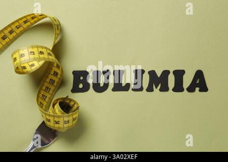 Word Bulimia, measuring tape and fork on olive background, top view Stock Photo