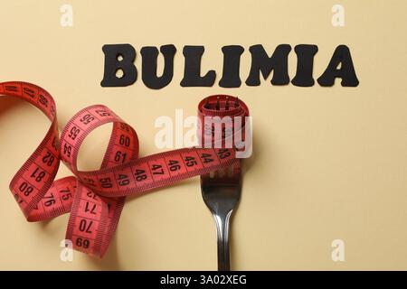 Word Bulimia, fork and measuring tape on beige background, top view Stock Photo